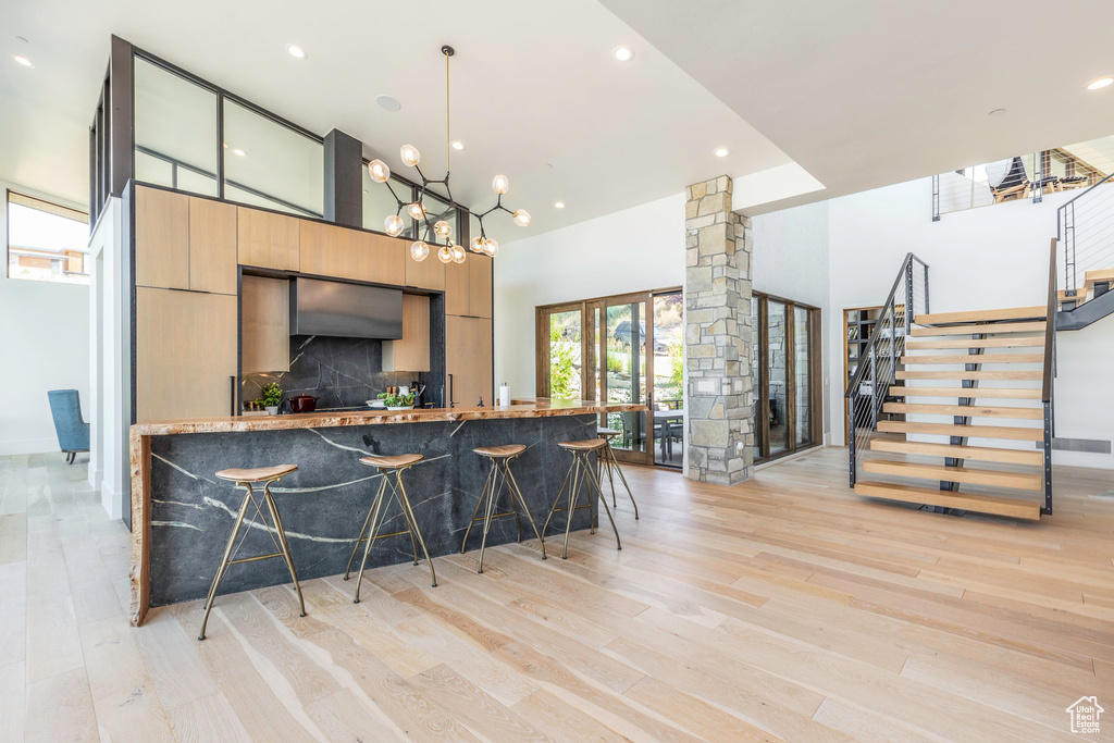 Interior space with a breakfast bar, hanging light fixtures, light hardwood / wood-style floors, a high ceiling, and light brown cabinetry