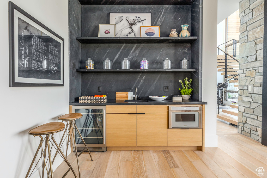 Bar featuring beverage cooler, light wood-type flooring, light brown cabinets, sink, and oven