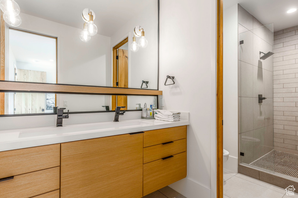 Bathroom featuring tile patterned floors, a shower with door, double vanity, and toilet