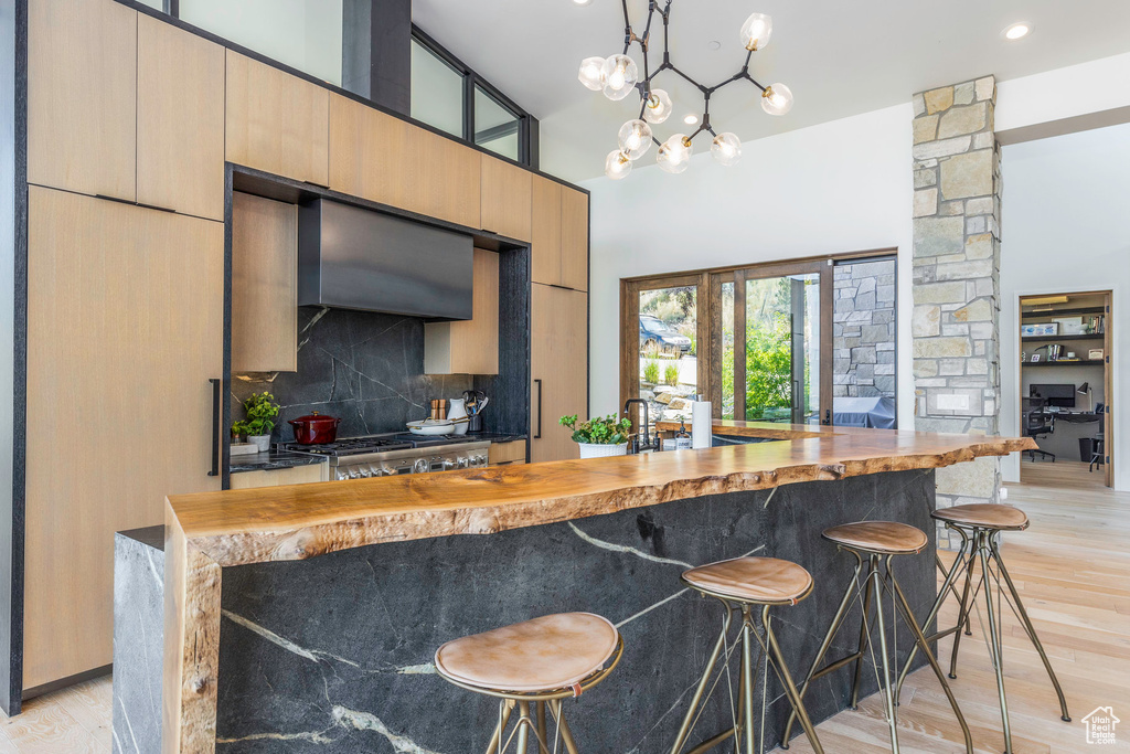 Interior space featuring light hardwood / wood-style flooring, wall chimney range hood, decorative backsplash, decorative light fixtures, and butcher block countertops