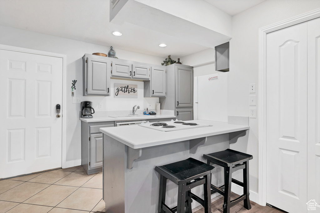 Kitchen featuring gray cabinets, light tile patterned floors, white appliances, a breakfast bar area, and kitchen peninsula