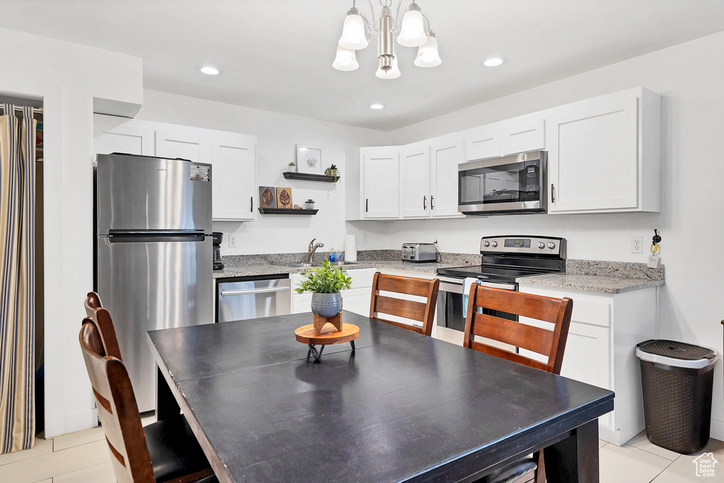 Kitchen featuring decorative light fixtures, white cabinetry, stainless steel appliances, light stone countertops, and light tile patterned floors