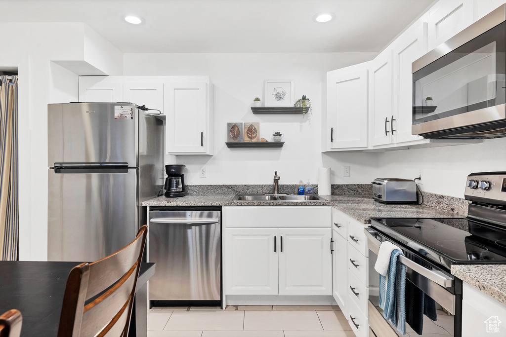 Kitchen featuring light tile patterned flooring, sink, appliances with stainless steel finishes, and white cabinets