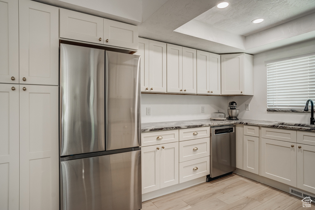 Kitchen featuring sink, light stone counters, stainless steel appliances, and white cabinetry