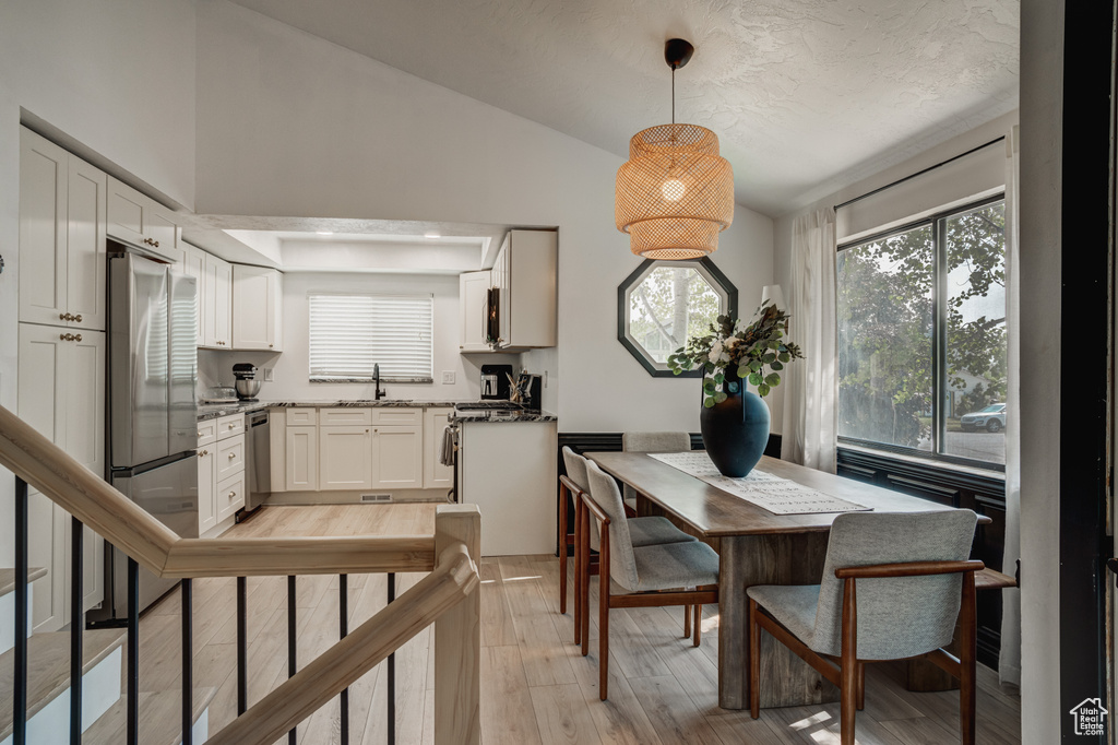 Dining room with light hardwood / wood-style floors, vaulted ceiling, and sink