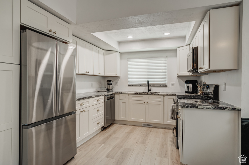 Kitchen with white cabinets, stainless steel appliances, dark stone counters, and light hardwood / wood-style flooring