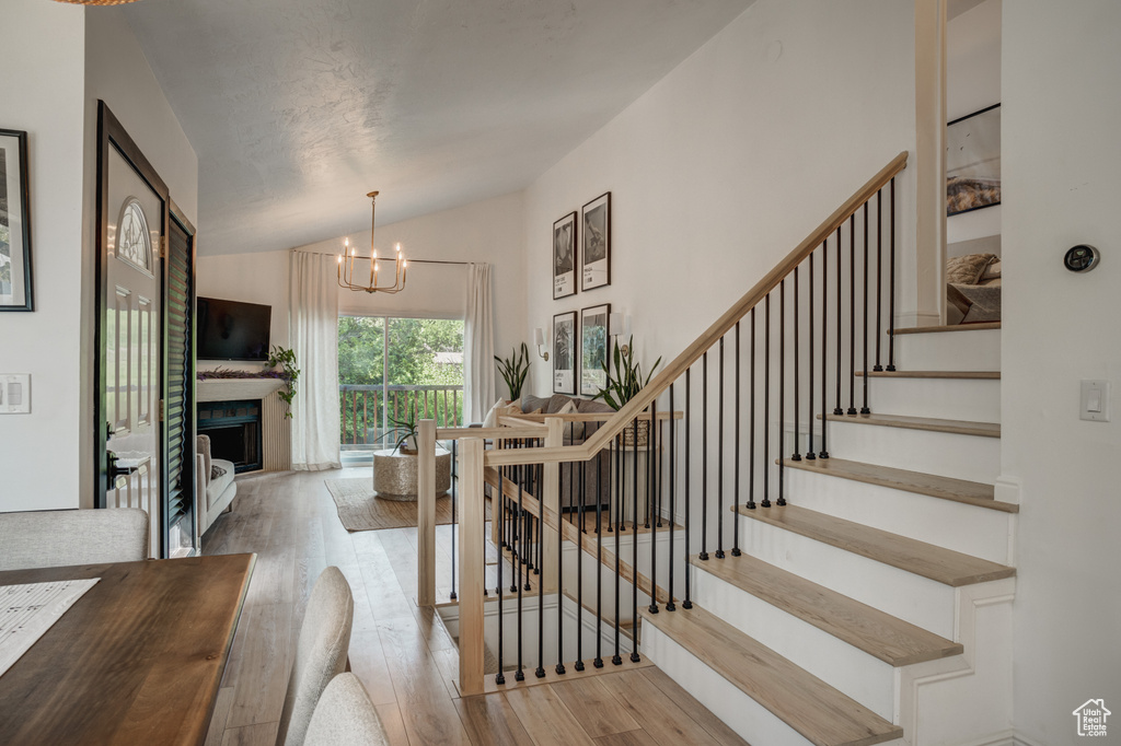 Stairs featuring light hardwood / wood-style floors, a notable chandelier, and vaulted ceiling