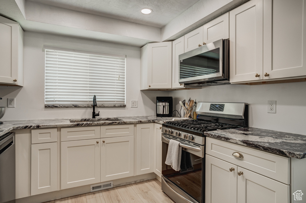 Kitchen with stainless steel appliances, sink, light hardwood / wood-style floors, stone countertops, and white cabinetry