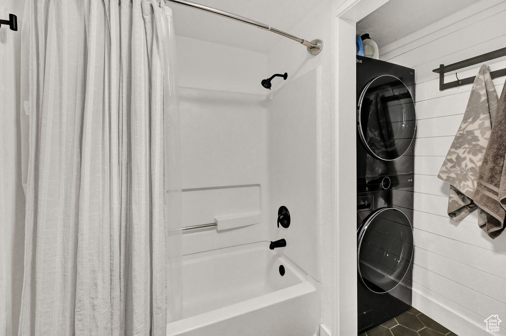 Bathroom with wood walls, tile patterned floors, shower / bath combo with shower curtain, and stacked washing maching and dryer