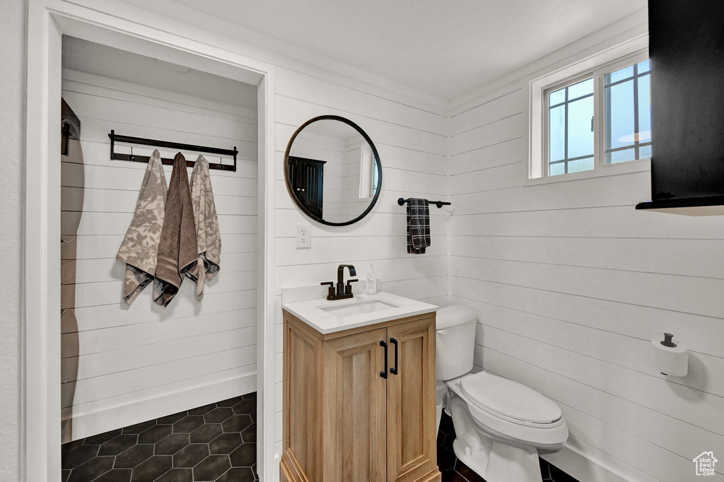 Bathroom with wooden walls, tile patterned flooring, toilet, and vanity