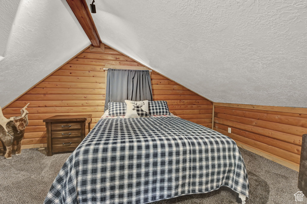 Unfurnished bedroom with vaulted ceiling, carpet, a textured ceiling, and log walls