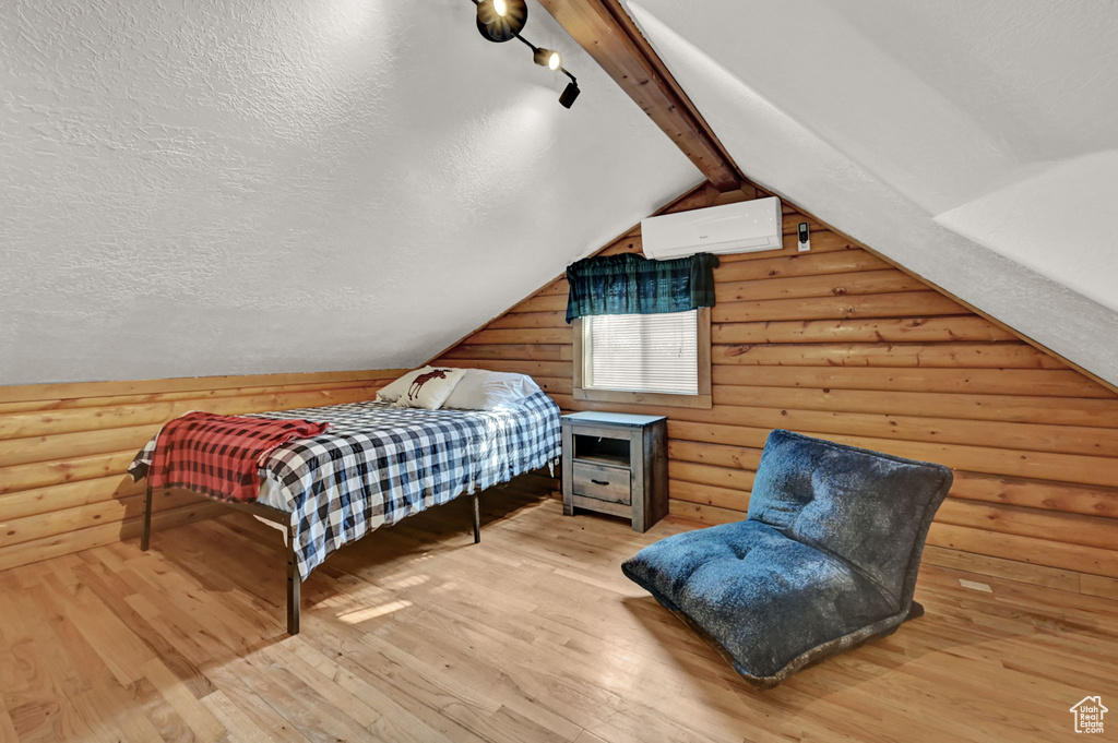 Bedroom with a wall mounted air conditioner, log walls, and light hardwood / wood-style floors