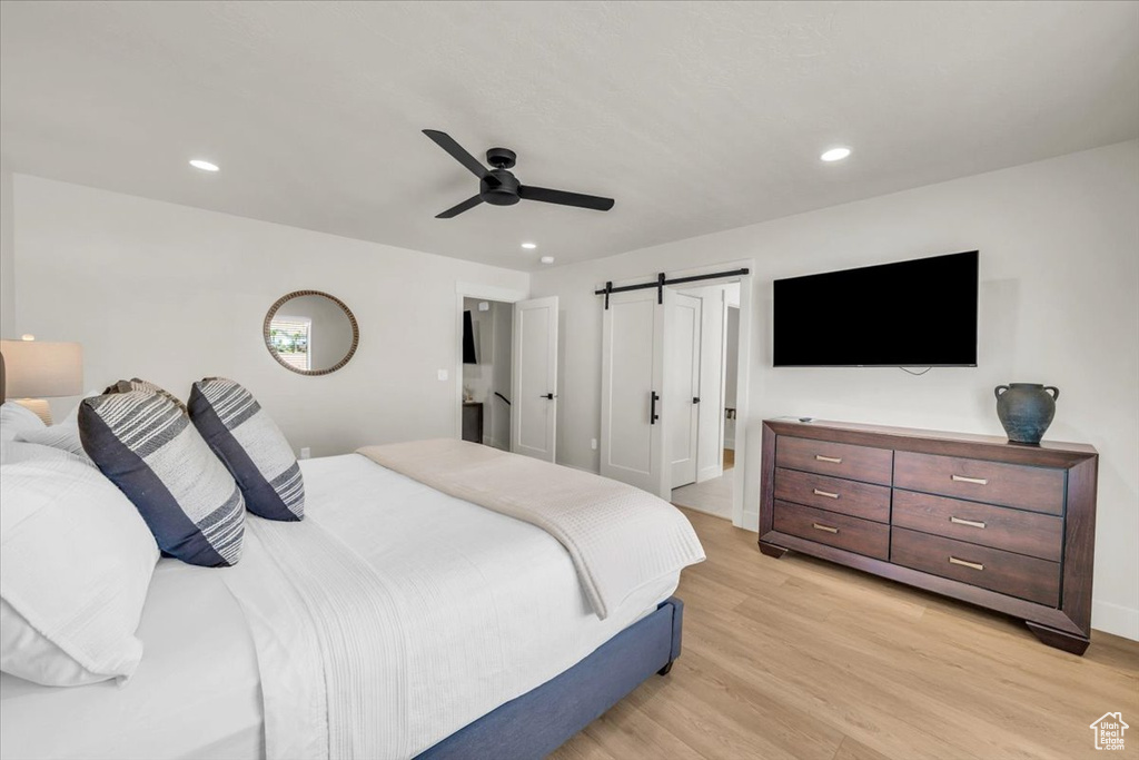 Bedroom featuring ensuite bathroom, light hardwood / wood-style flooring, a barn door, and ceiling fan