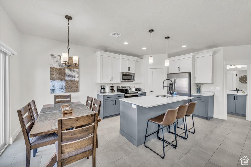 Kitchen with a breakfast bar, hanging light fixtures, appliances with stainless steel finishes, and gray cabinetry