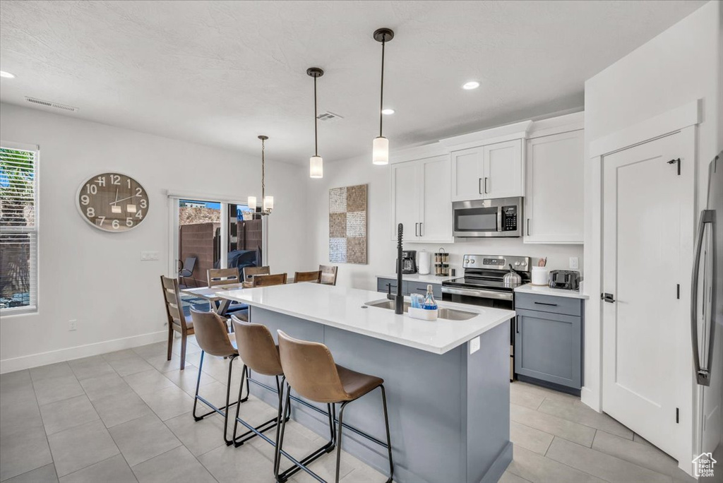 Kitchen featuring light tile patterned floors, white cabinets, hanging light fixtures, appliances with stainless steel finishes, and sink