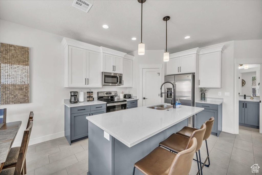 Kitchen with white cabinets, stainless steel appliances, sink, decorative light fixtures, and light tile patterned floors