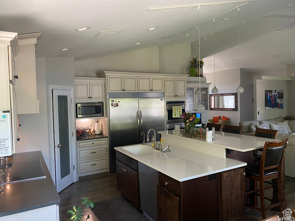 Kitchen featuring dark hardwood / wood-style flooring, a kitchen island with sink, built in appliances, vaulted ceiling, and sink