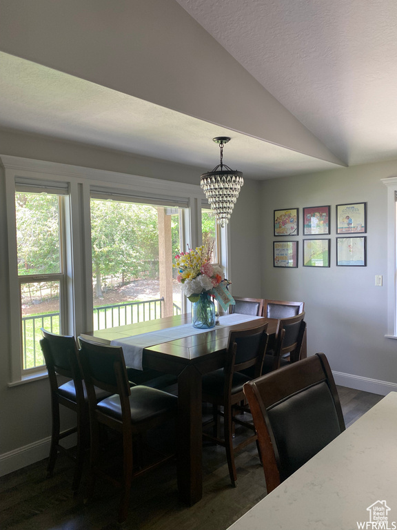 Dining area with a notable chandelier, a wealth of natural light, vaulted ceiling, and dark wood-type flooring