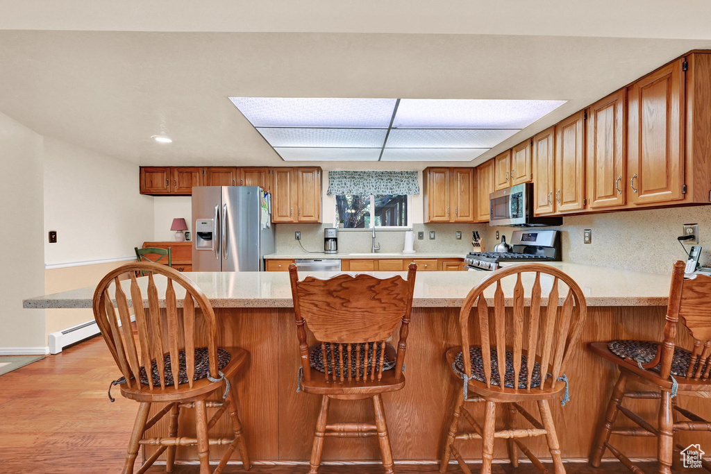 Kitchen with appliances with stainless steel finishes, kitchen peninsula, and light hardwood / wood-style flooring