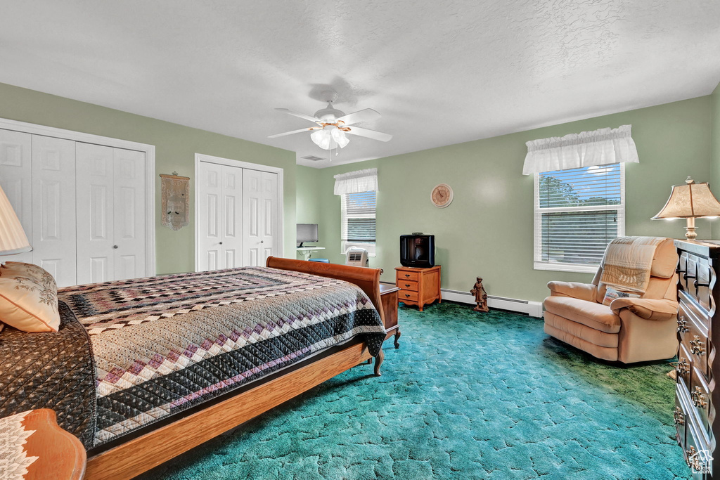 Bedroom with two closets, carpet, ceiling fan, and a baseboard heating unit