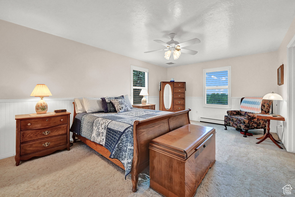 Carpeted bedroom with a baseboard heating unit, multiple windows, and ceiling fan