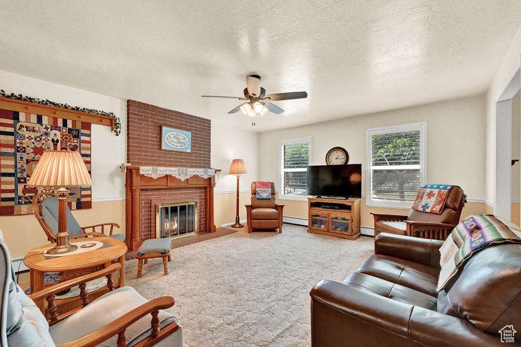 Living room with a textured ceiling, ceiling fan, light colored carpet, a brick fireplace, and brick wall