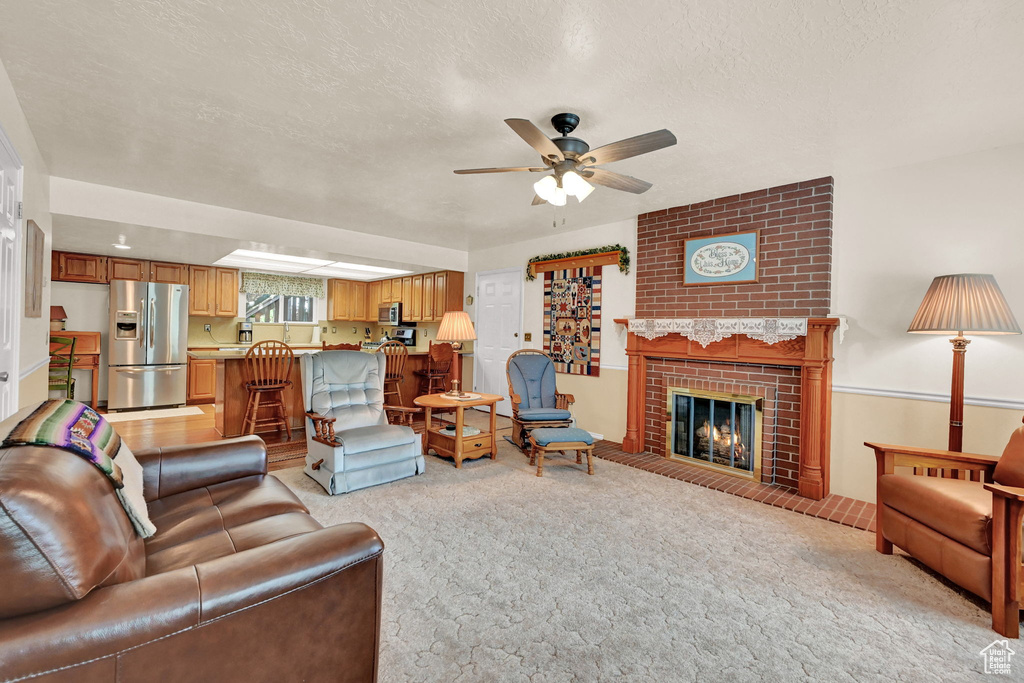 Carpeted living room featuring brick wall, a fireplace, a textured ceiling, and ceiling fan