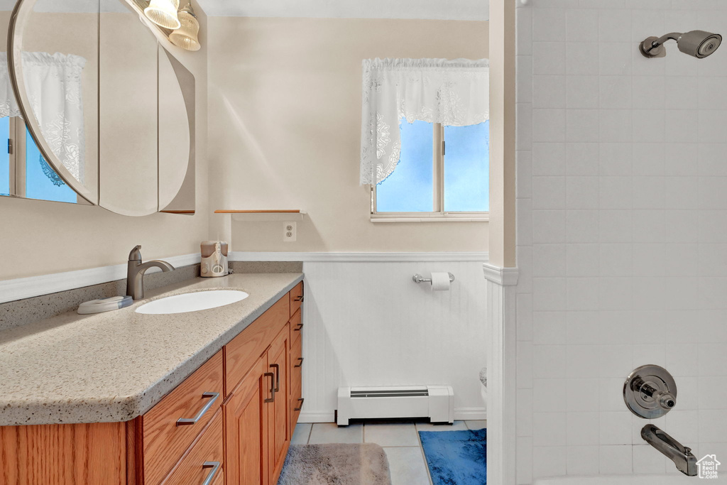 Bathroom with tiled shower / bath combo, vanity, baseboard heating, and tile patterned flooring