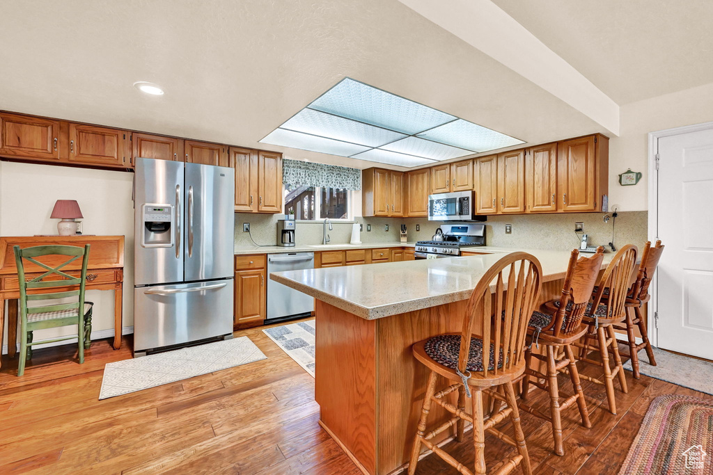 Kitchen with a kitchen bar, appliances with stainless steel finishes, kitchen peninsula, and light hardwood / wood-style flooring