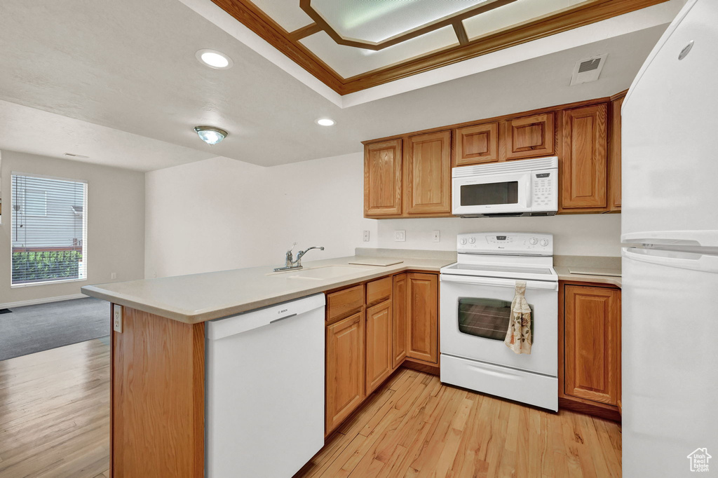 Kitchen with sink, white appliances, light wood-type flooring, and kitchen peninsula