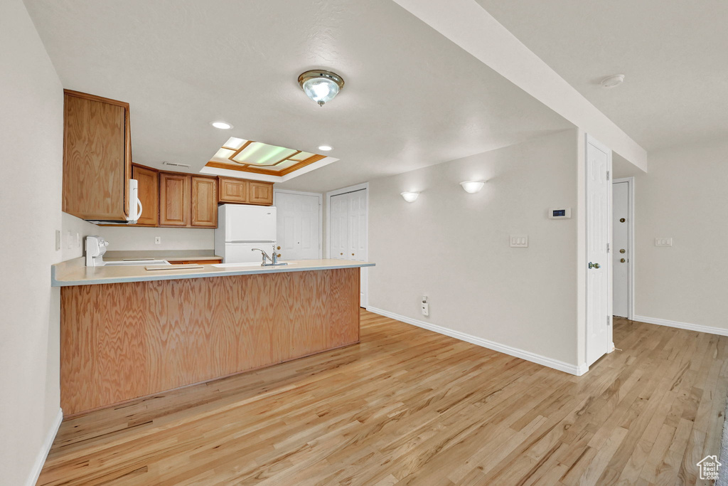 Kitchen with light wood-type flooring, kitchen peninsula, white appliances, and a skylight