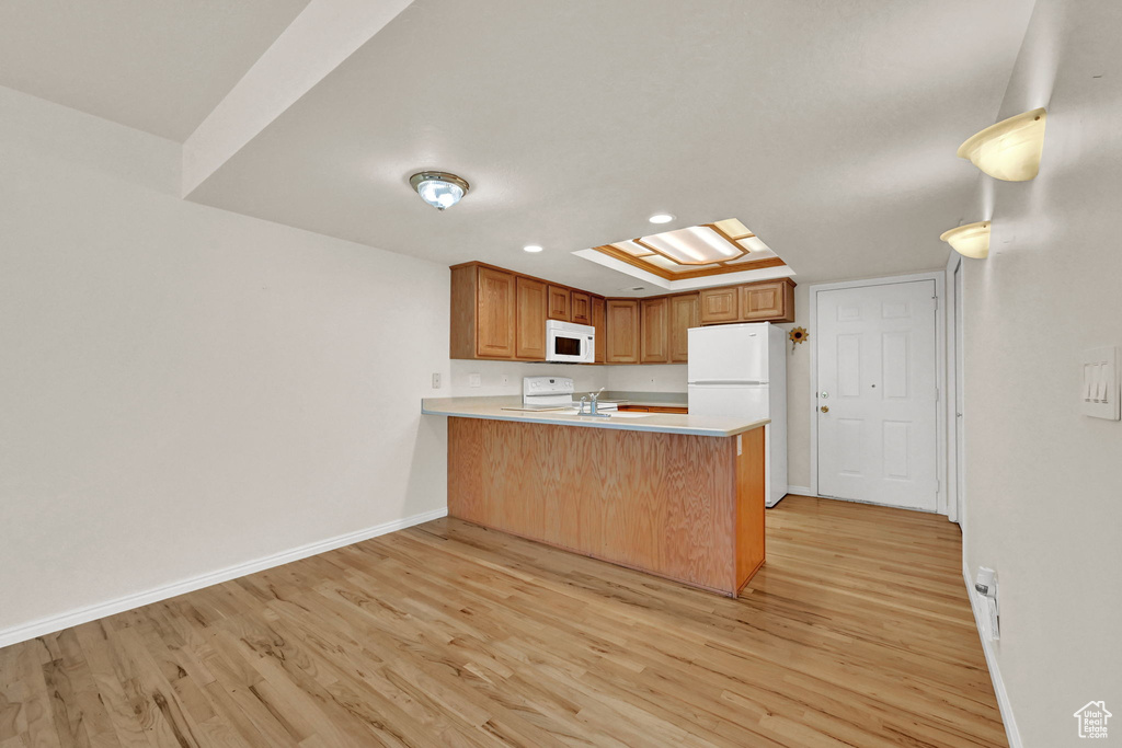 Kitchen with a skylight, light hardwood / wood-style flooring, kitchen peninsula, and white appliances