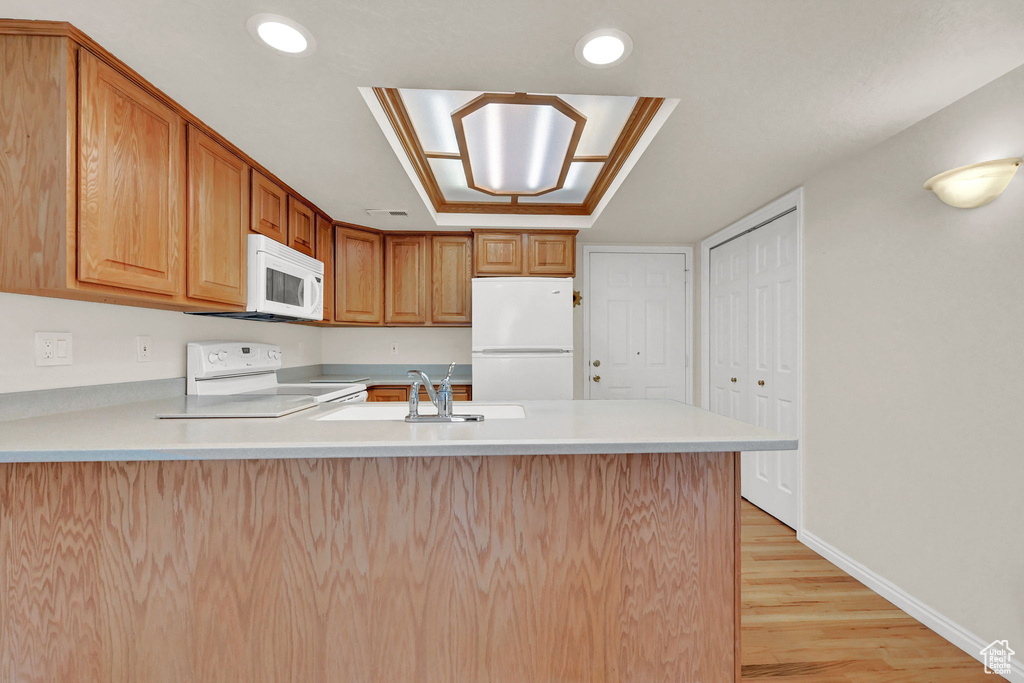 Kitchen featuring sink, kitchen peninsula, light wood-type flooring, and white appliances