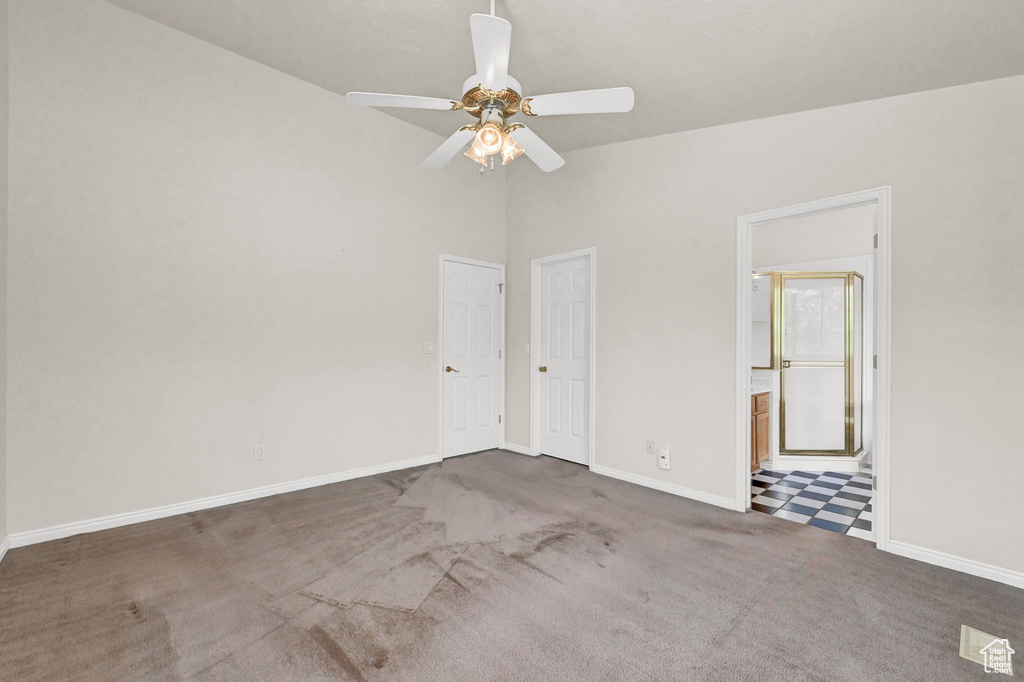 Unfurnished room with dark colored carpet, ceiling fan, and vaulted ceiling