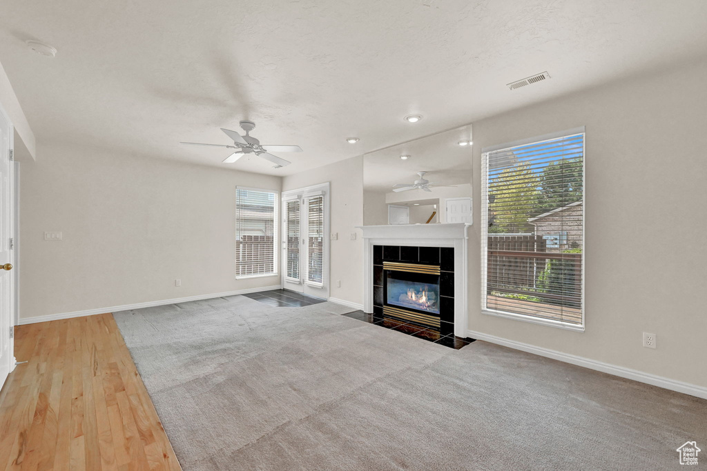 Unfurnished living room with a tiled fireplace, ceiling fan, and light colored carpet