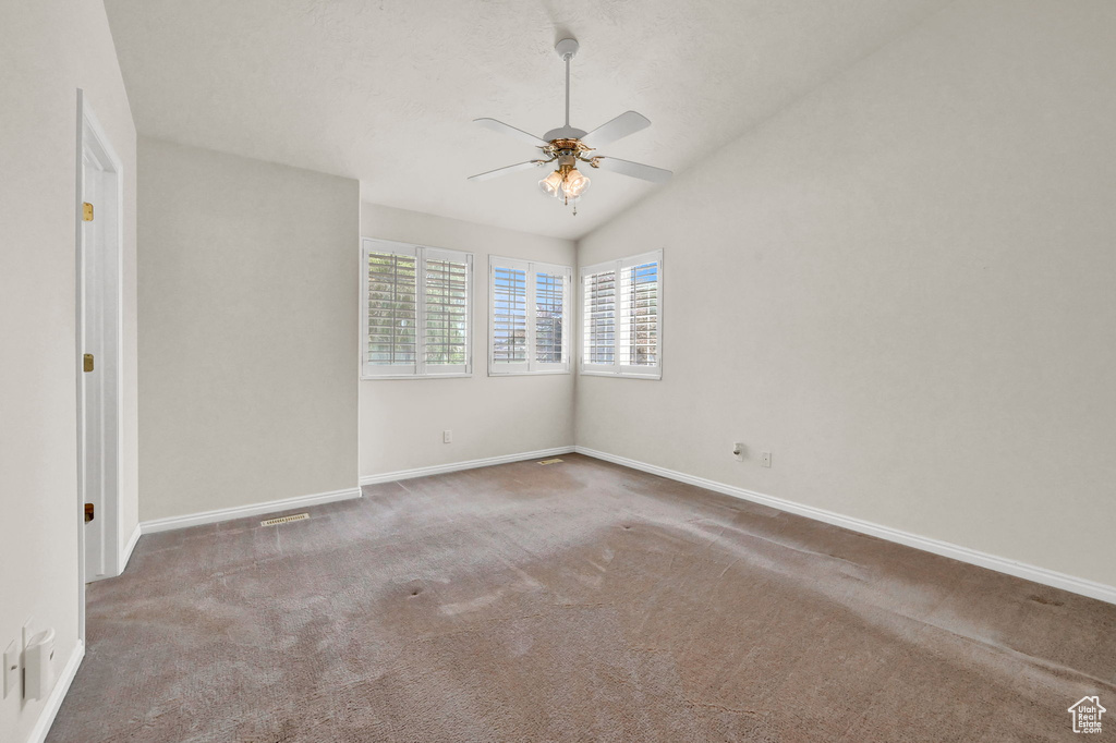 Carpeted empty room with ceiling fan and lofted ceiling