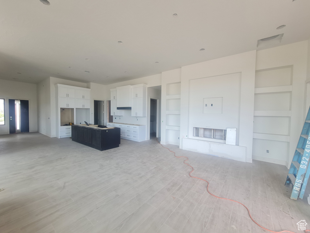 Unfurnished living room with built in shelves and light wood-type flooring