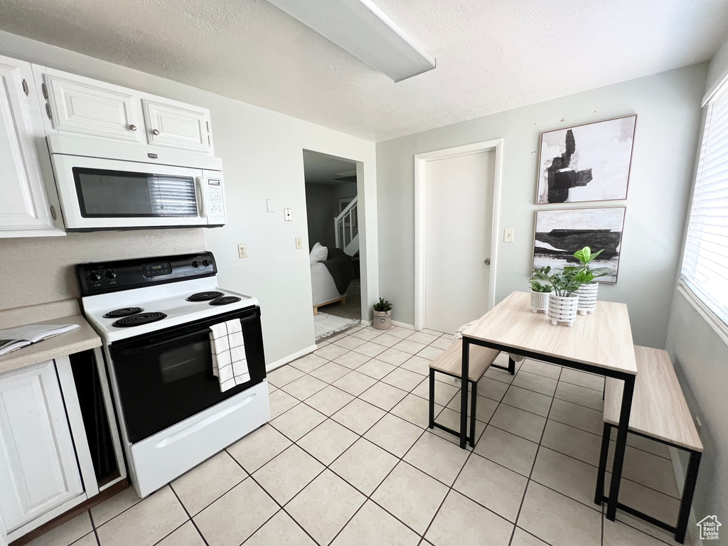 Kitchen with light tile patterned flooring, white appliances, and white cabinetry