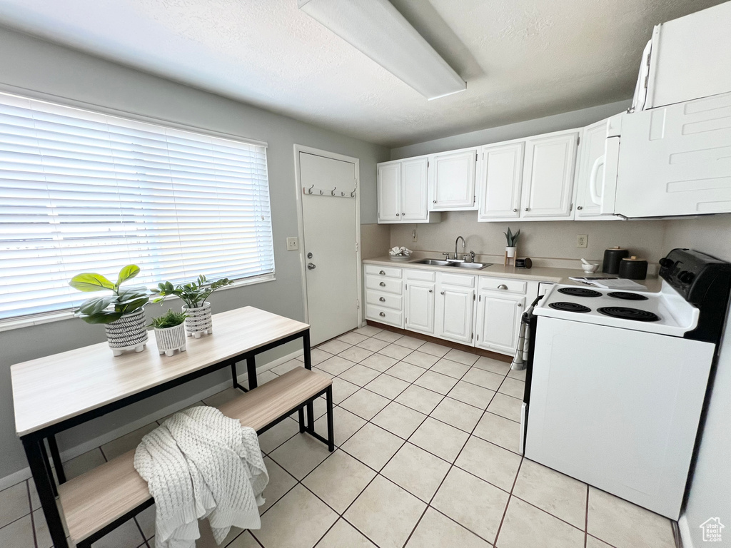 Kitchen featuring white appliances, sink, light tile patterned flooring, and white cabinetry