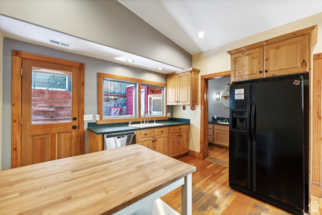 Kitchen featuring vaulted ceiling, sink, stainless steel dishwasher, light wood-type flooring, and black fridge with ice dispenser