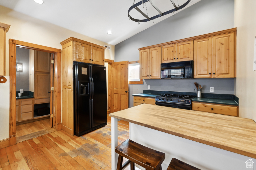 Kitchen featuring butcher block countertops, light hardwood / wood-style flooring, black appliances, a breakfast bar, and lofted ceiling