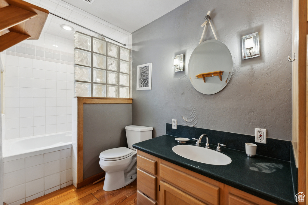 Full bathroom with vanity, tiled shower / bath combo, toilet, and hardwood / wood-style floors