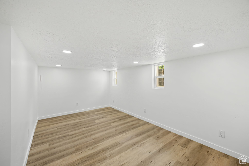 Basement with light wood-type flooring and a textured ceiling