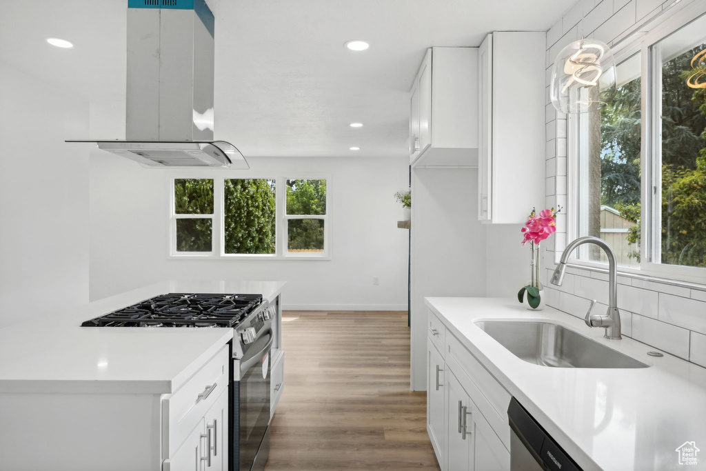 Kitchen featuring white cabinetry, stainless steel gas stove, island exhaust hood, wood-type flooring, and sink