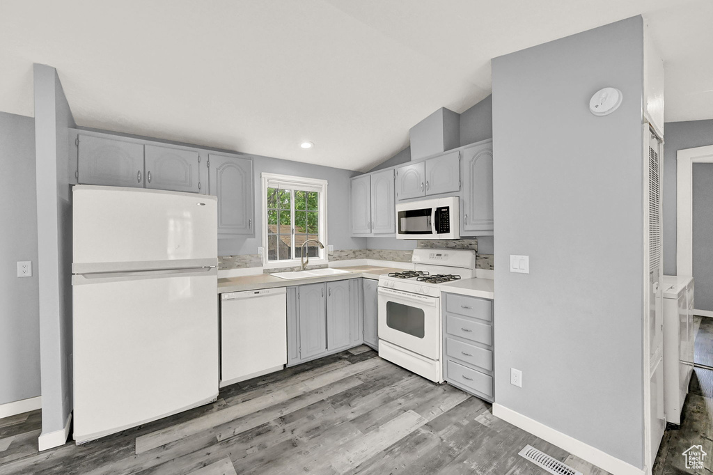 Kitchen featuring lofted ceiling, white appliances, light hardwood / wood-style floors, sink, and gray cabinetry