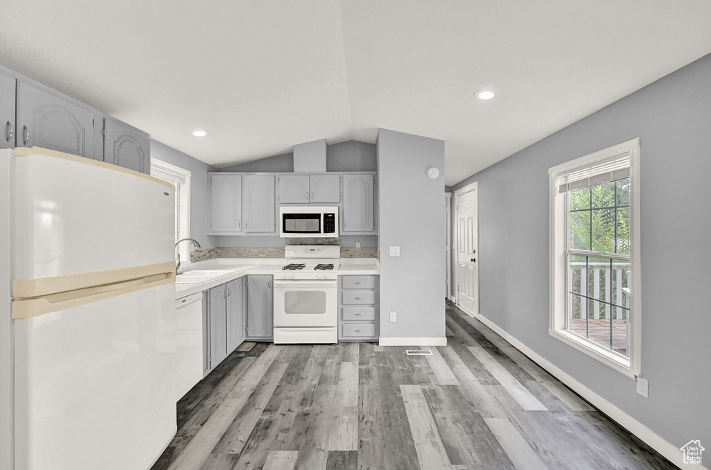 Kitchen featuring wood-type flooring, white appliances, sink, lofted ceiling, and gray cabinetry