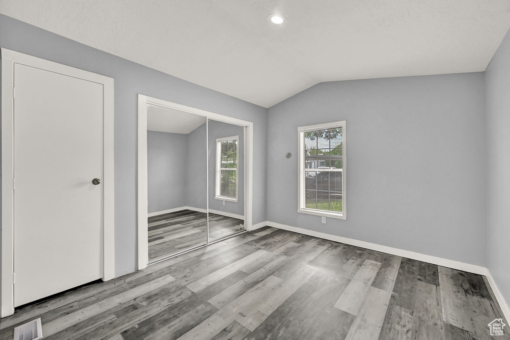 Empty room with hardwood / wood-style flooring and vaulted ceiling