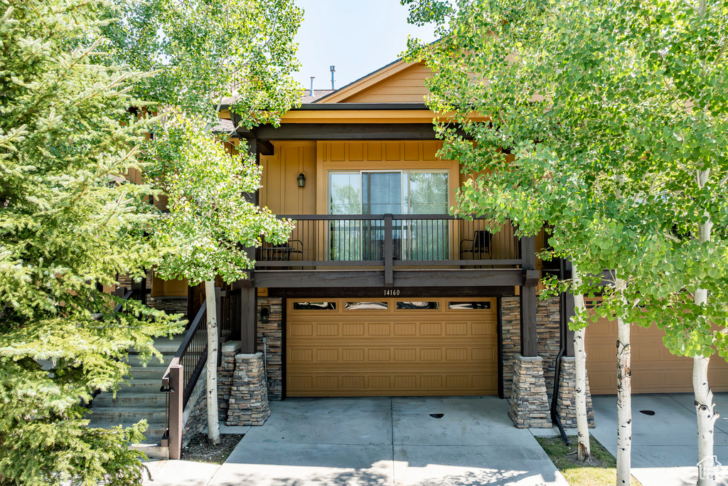 View of front of house with concrete driveway, a garage, stone siding, and a balcony