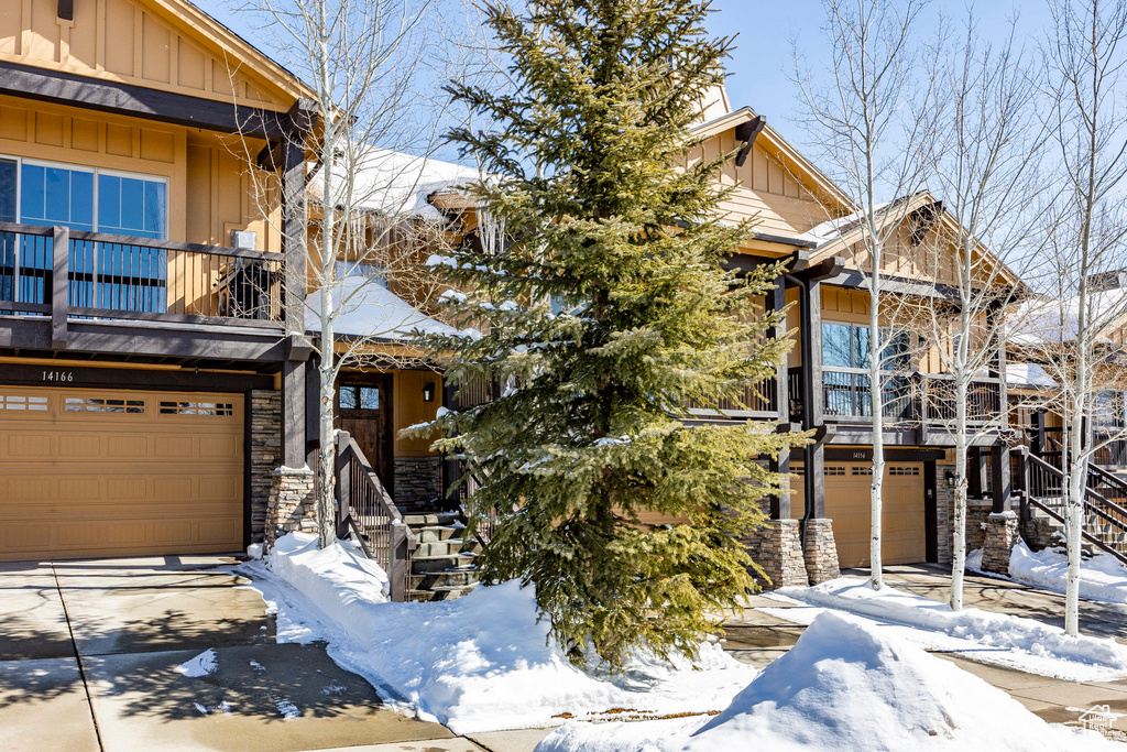 View of front of home featuring a balcony, driveway, stone siding, board and batten siding, and a garage