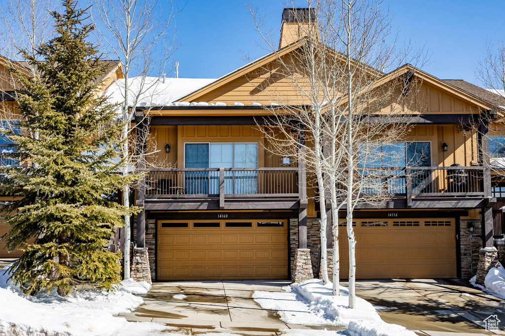 View of front of property with a garage, a balcony, stone siding, and concrete driveway